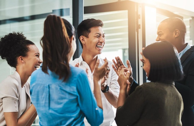Un groupe de cinq personnes souriantes échange des rires et des applaudissements dans un environnement lumineux et moderne. Ils expriment de la joie et de l'enthousiasme lors d'une interaction amicale.